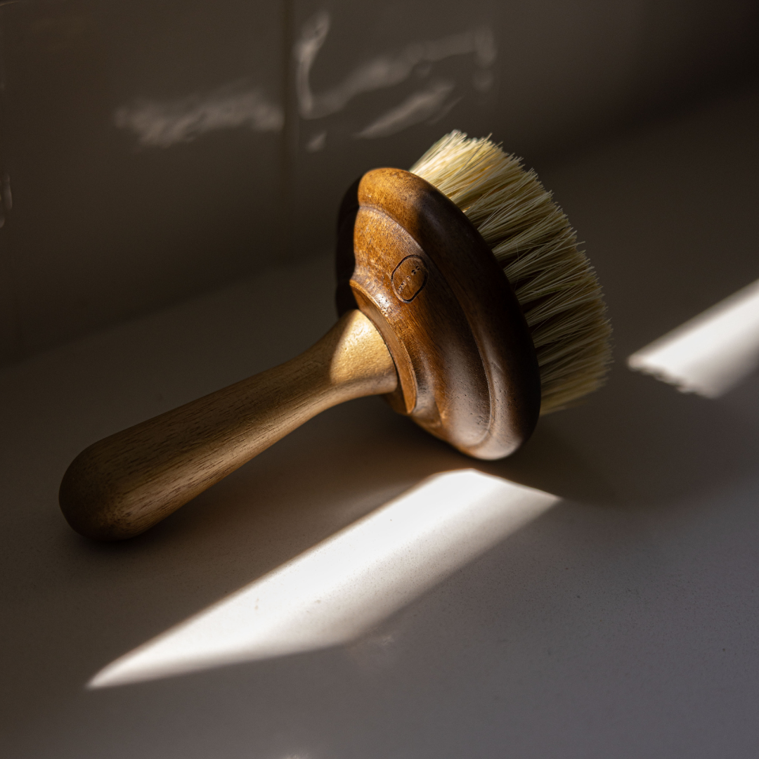 Brosse en bois présentée avec sur un plan de travail clair, mise en scène déco de cuisine avec rayon de soleil.