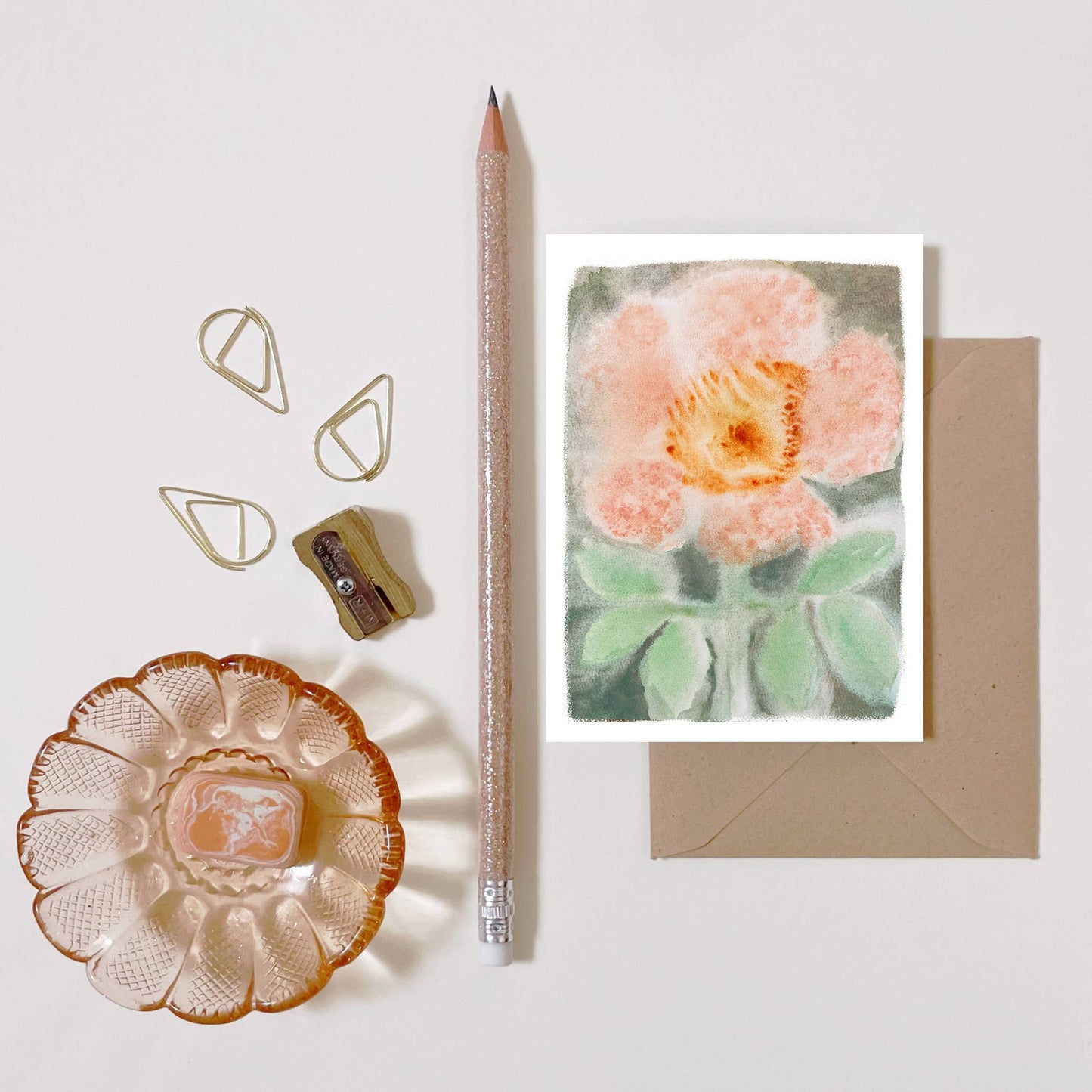 Carte illustrée d'une églantine imprimée sur papier certifié FSC au style botanique et champêtre., posé sur fond blanc avec un crayon, un taille crayon et une coupelle