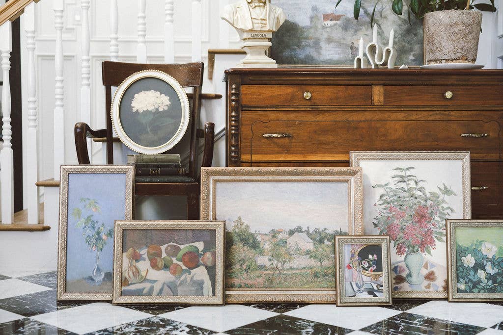 ensemble d'oeuvres imprimées et encadrées impressionnistes, posées sur un sol à damier devant une commode en bois ancienne
