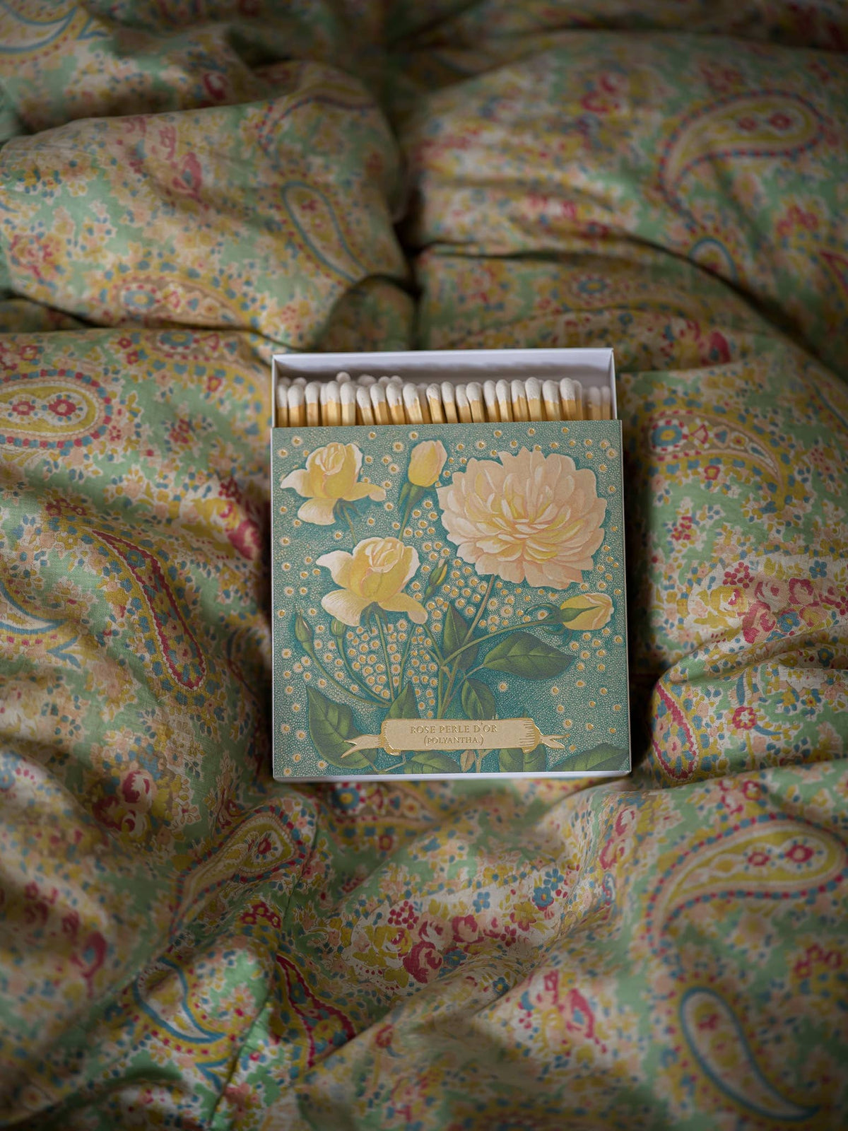 Allumettes grand format avec boîte fleurie posée sur une couette fleurie