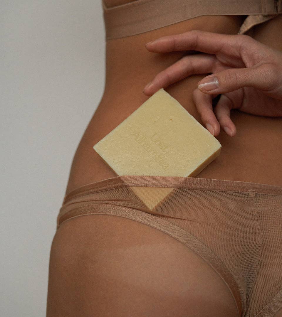 savon doux aux huiles végétales pour la peau. Image du savon contre la peau et une main voulant l'attraper