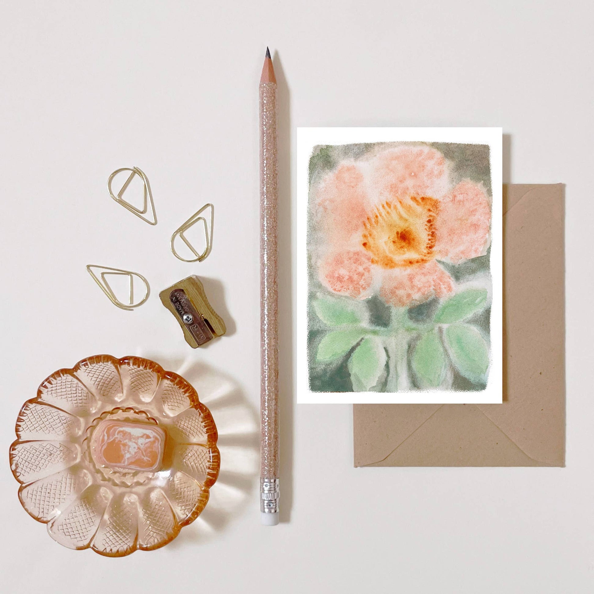 Carte illustrée d'une églantine imprimée sur papier certifié FSC au style botanique et champêtre., posé sur fond blanc avec un crayon, un taille crayon et une coupelle