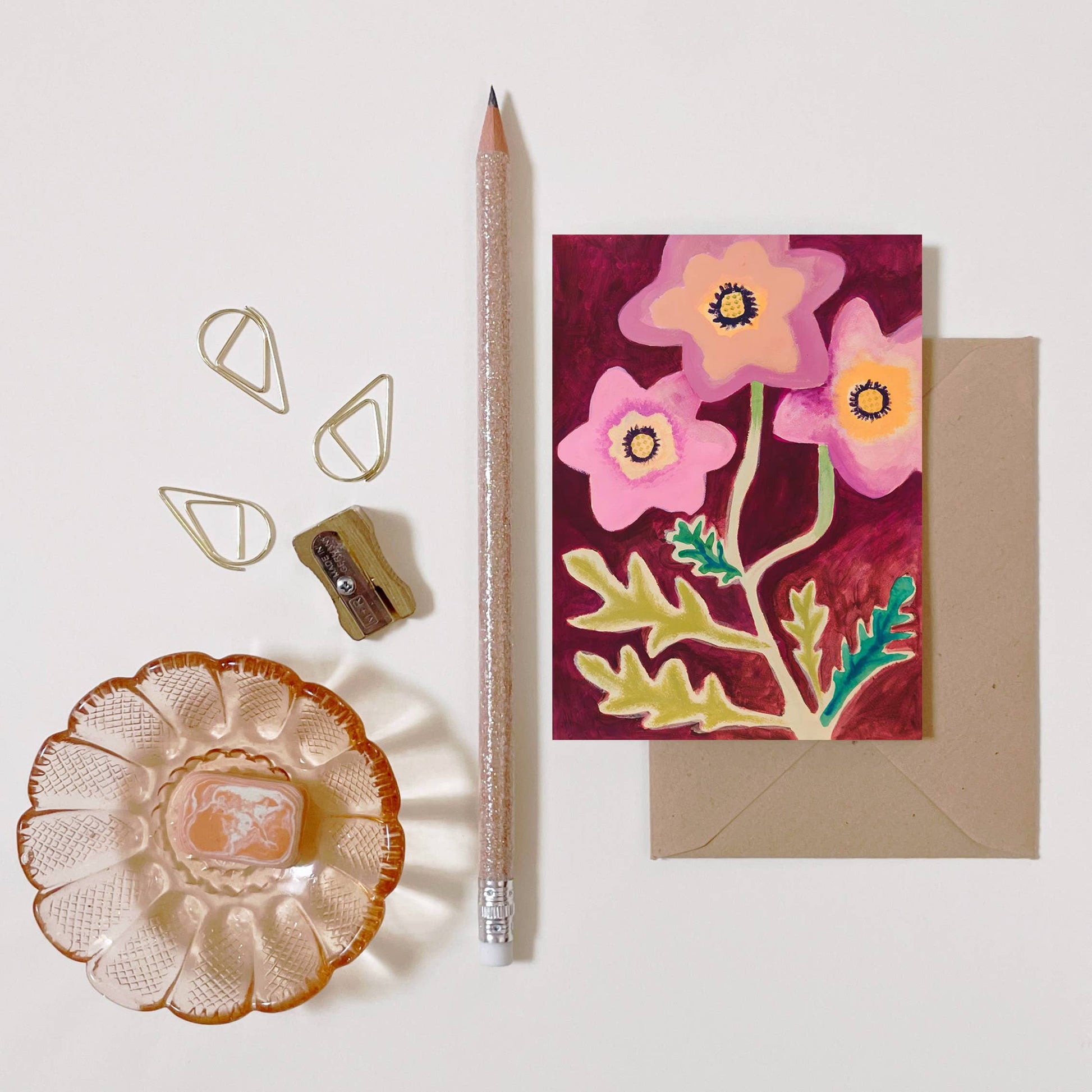 mini carte de voeux fleurie avec son enveloppe, posées sur un bureau avec un crayon, un taille crayon et une coupelle
