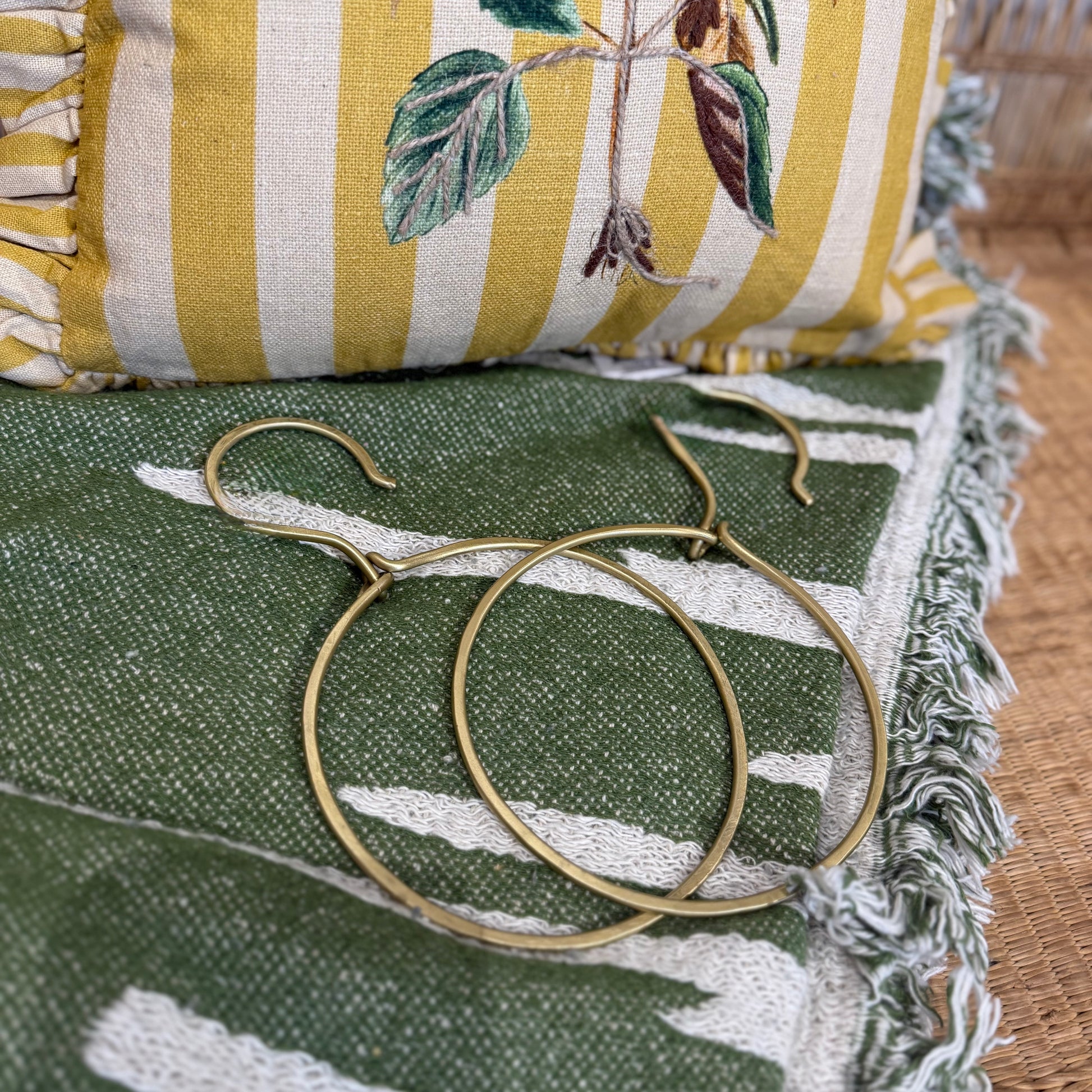 cintres dorés ronds posés sur le plaid Haxby  vert avec le coussin camila à  rayures jaunes et crème à l'arrière