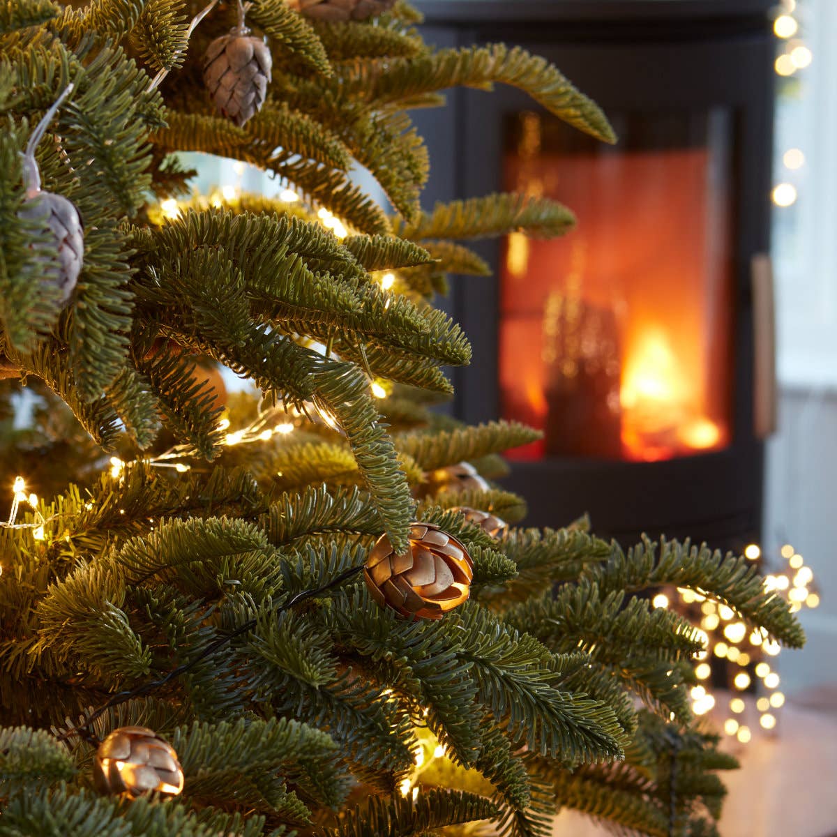 Guirlande dorée avec LED blanc chaud sur sapin, cheminée en fond, ambiance naturelle et chic.