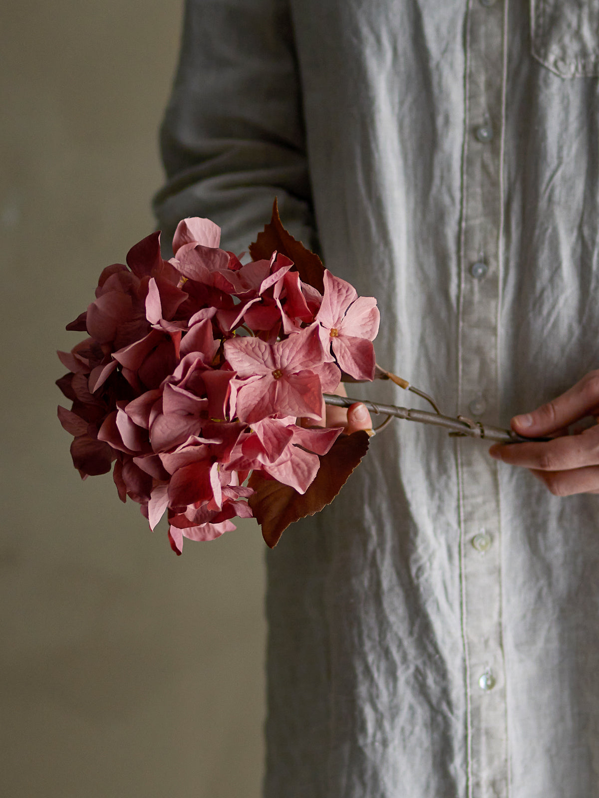 Tige d’hortensia artificiel rose de 65 cm avec grande fleur réaliste de 20 cm de diamètre tenu par les mains d'une femme
