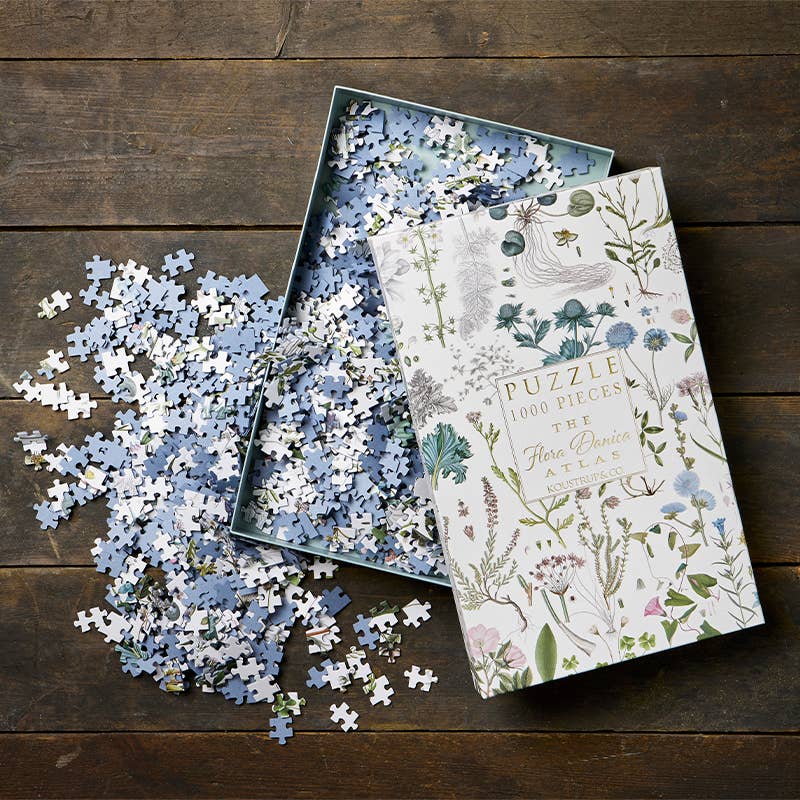 Puzzle de 1000 pièces illustré de plantes et fleurs sauvages issues de Flora Danica, célèbre atlas botanique danois. Fabriqué en Europe. Boîte ouverte sur une table en bois