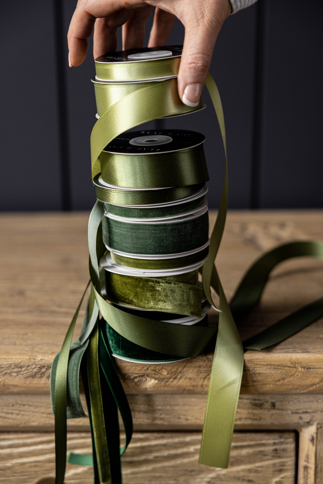 empilement de rubans verts pour cadeaux et une main posant sur la pile un ruban en satin vert.