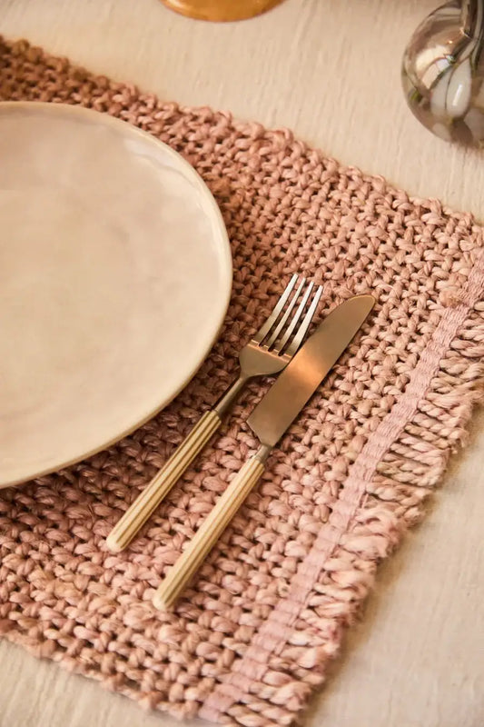 set de table en jute rose avec une assiette beige posée dessus et des couverts avec des rayures