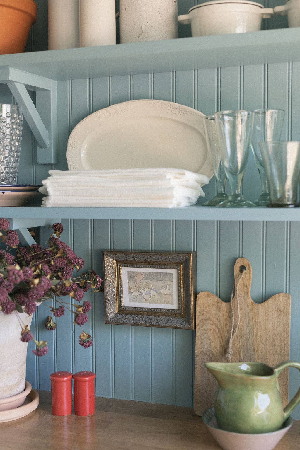 Petit tableau des oies dans le jardin accroché sur un mur en bois bleu gris dans une cuisine de style campagne. Madame Beaumont