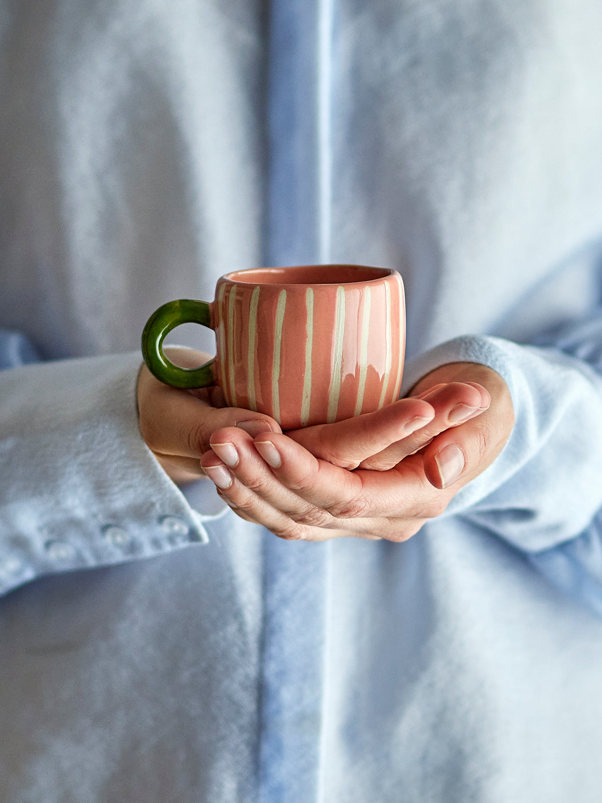 Petite tasse Nini en grès brillant à rayures en relief et anse ronde verte, contenance 100 ml dans les mains d'une femme
