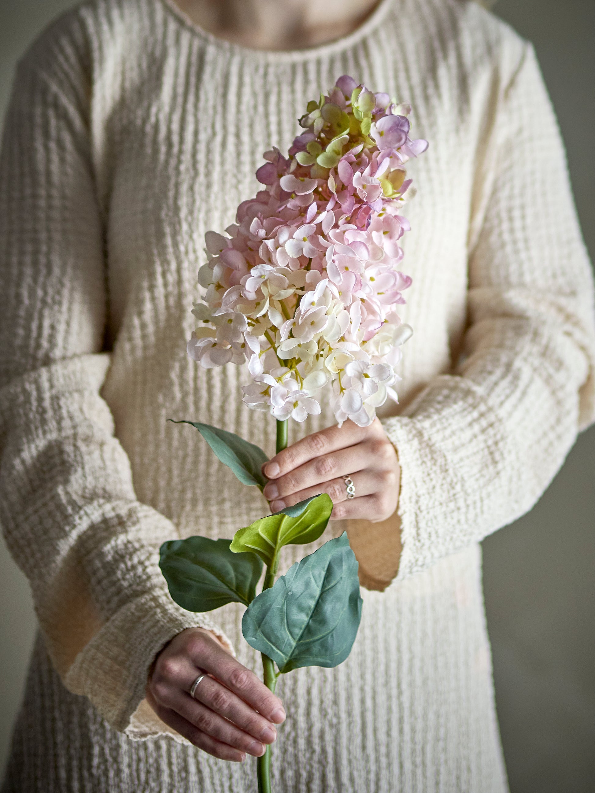 Tige d’hortensia artificielle Bloomingville rose et blanche, fleur décorative élégante pour vase et bouquet campagne chic. Tenue par une femme dans les mains.