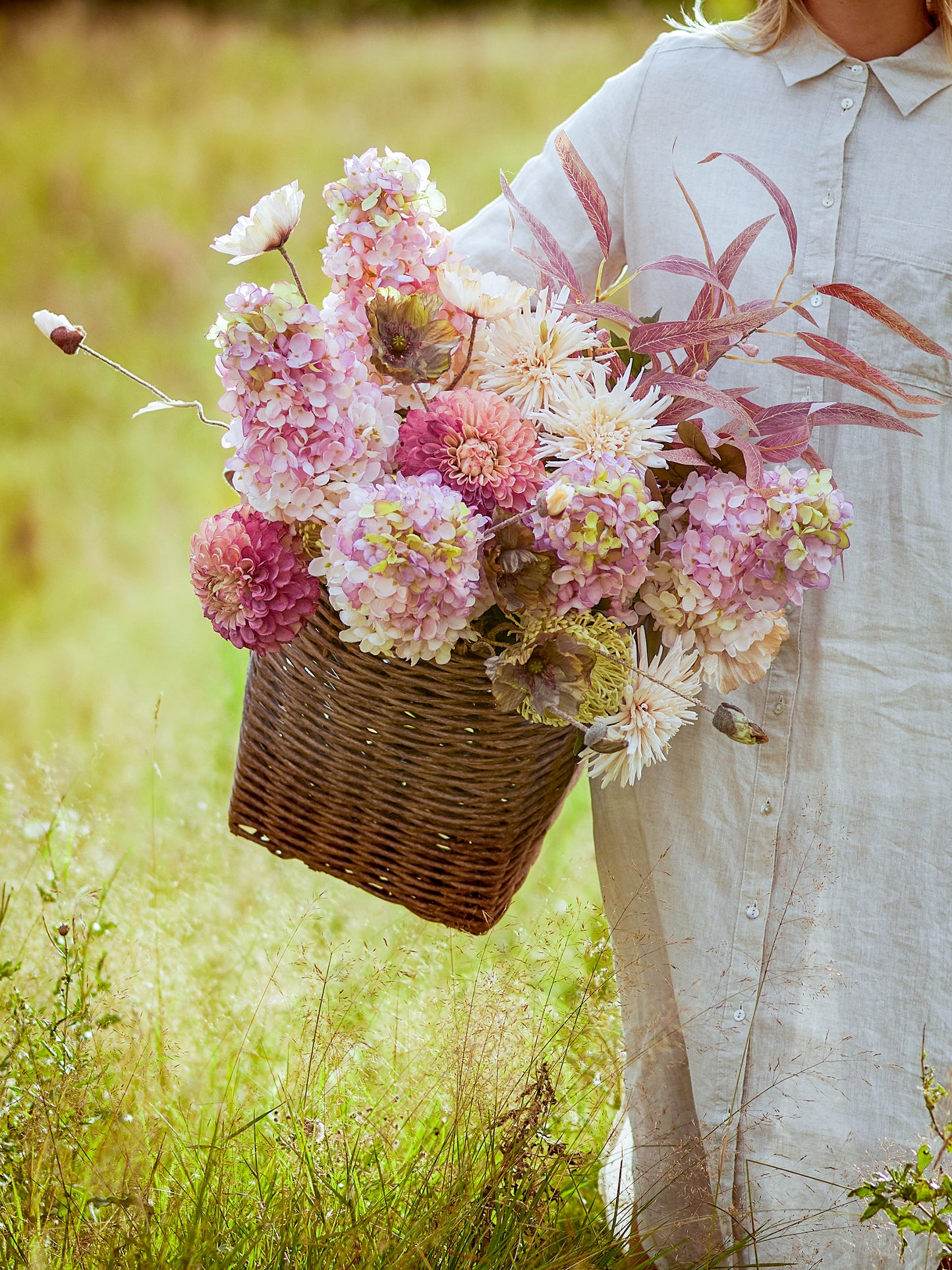 Composition florale avec tiges d’hortensia artificielles roses dans un panier en osier, ambiance romantique campagne chic.